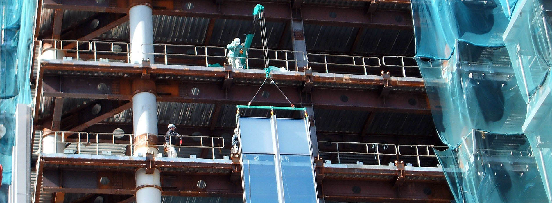 Mini grúa MAEDA elevando un marco de cristal para la instalación de muros cortina