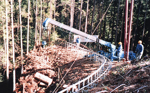 Mini grúa MAEDA levantando madera cortada para un proyecto forestal